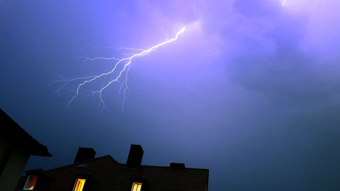Blitze entladen sich während eines Gewitters über einem Wohnhaus.